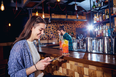 A girl with  cocktail smiles with tablet behind counter at the bar.の写真素材