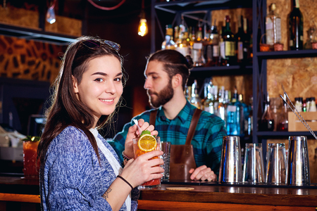 A girl with  cocktail smiles behind counter at the bar.の写真素材