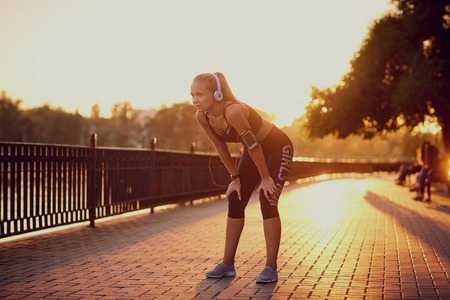 Girl in headphones on a run in the park at sunset.の写真素材