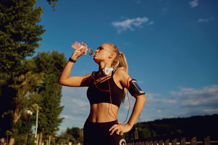 Girl runner drinks water from a bottle in the park. Healthy lifestyle.の写真素材