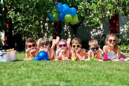Group of children in sunglasses smiling lies on grass in summer.の写真素材