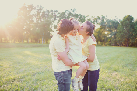 Parents kiss and hug their daughter in the park in the summer.の写真素材