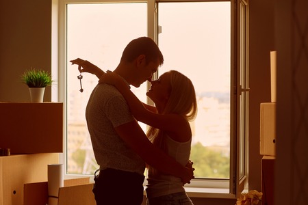 Young couple with keys in new apartment house. Silhouettes. The concept of moving, housewarming.の写真素材