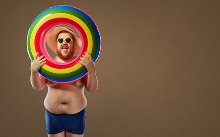 Thick funny man smiling in a swimsuit with an inflatable circle. The concept of summer holidays with humor is fun.の写真素材