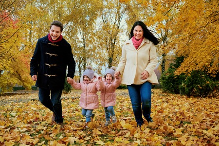 Happy family playing in autumn park. Parents with children run in the nature on yellow leaves.の写真素材
