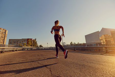 A woman runner jogs on a bridge in the city.の写真素材