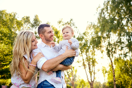 Happy family in a park in summer autumn. Mother, father and baby play in nature in the rays of sunset.の写真素材