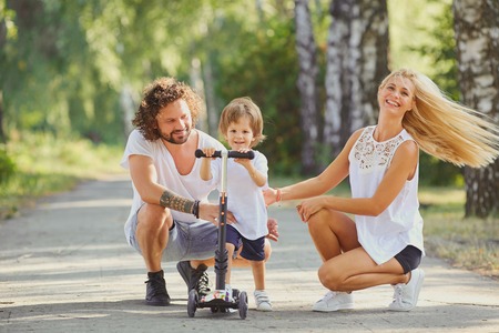 Happy family in the park. Parents with a child on a scooter are walking in nature.の写真素材