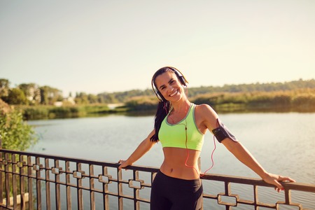 Spanish girl running in headphones smiling at lake in park.の写真素材