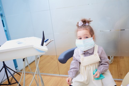 A little girl wearing a mask in the dentist's office.の写真素材