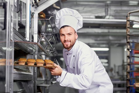 A man baker with a tray of cupcakes in a bakery.の写真素材