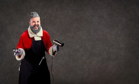 Santa Claus hairdresser barber with scissors and a hair dryer in his hands on the background of copyspace.の写真素材