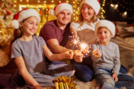 Family with Bengal lights in the room with a Christmas tree and a fireplace on Christmas Day.の写真素材