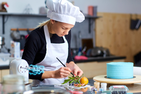 A confectioner woman decorates a cake on a table in the kitchen in a pastry shop.の写真素材