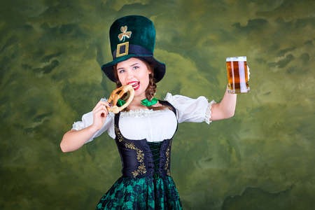 A girl in a St. Patrick costume with a mug of beer is smiling on a green background.の写真素材