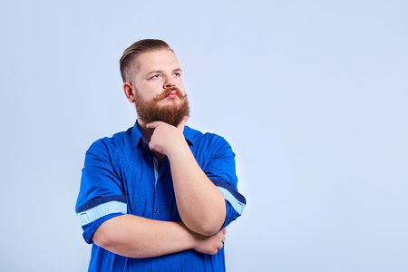 A fat, bearded man looks at the gray background with a thoughtful expression of emotion.の写真素材