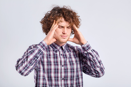 Curly young man holding his head with negative emotions on his face on a gray background.の写真素材