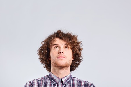 A curly-haired guy thinks with a serious emotion on a gray background.の写真素材