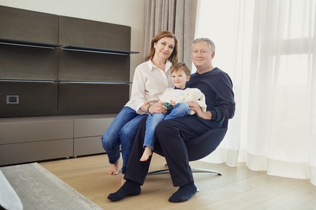 Grandmother and grandfather with grandson in an armchair in a room in front of a window. A happy family.の写真素材