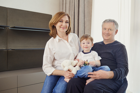 Grandmother and grandfather with grandson in an armchair in a room in front of a window. A happy...