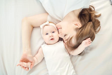 Top view of a happy mother kissing a baby lying on a bed indoors.