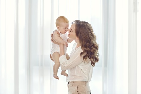 Mother with a baby in her arms plays against the window. Mothers Day.
