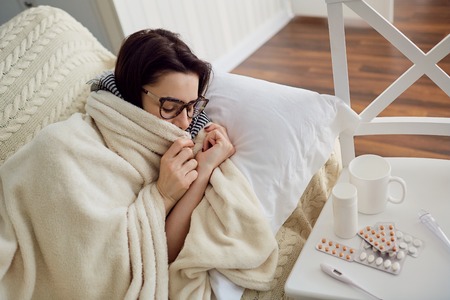 A chill woman under the blanket on the bed in the room. Seasonal viruses.