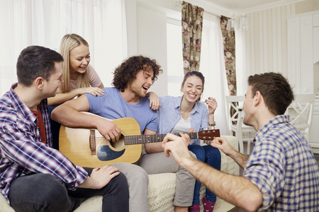A group of friends with a guitar sing fun songs at a party indoor.の写真素材