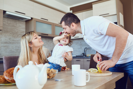 A happy family is eating in the kitchen while sitting at a table.の写真素材