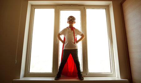 The boy in the costume of a superhero at the window.の写真素材