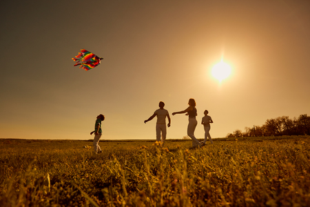 Happy family with a kite playing at sunset in the field.の写真素材