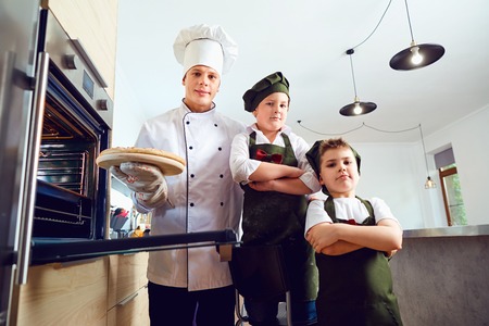 Children bakers with pizza in the kitchen with a cook.の写真素材