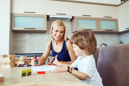 Mother and son draw on paper at a table inside the room.の写真素材