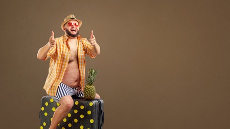 A funny fat man riding a suitcase on a summer vacation against a background for text.の写真素材