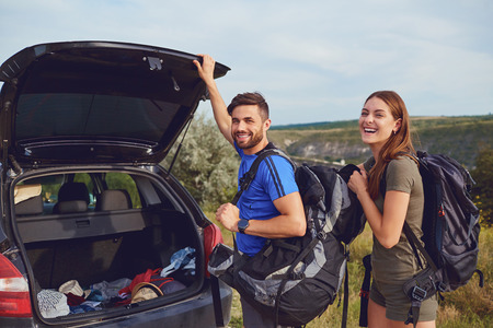 A couple of tourists with backpacks near a car on a background of nature.