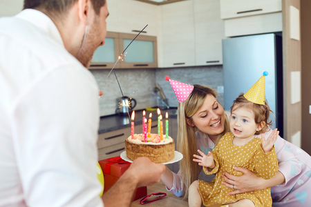 A family with a cake congratulates a happy child on his birthday. Happy parents congratulate their daughter.の写真素材