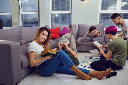 A female student reads a book against the background of friends in the room.の写真素材