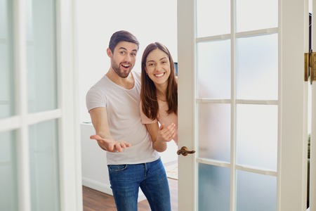 A happy couple with smiles opens the door to their house.の写真素材