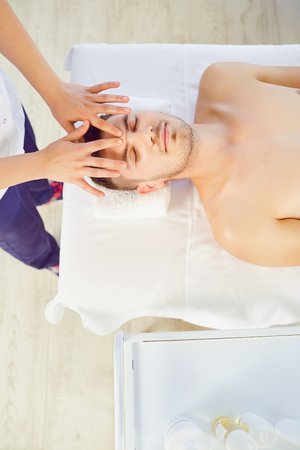 Facial massage for man. Hands of the massage therapist make a relaxing face massage to a man in a massage room.の写真素材