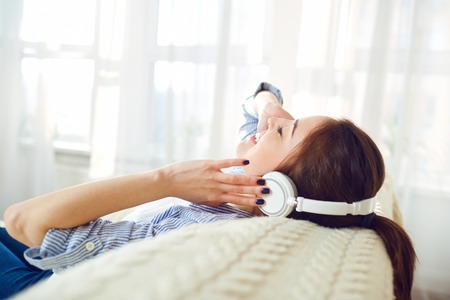 Girl in headphones smiling listening to music sitting in the room.の写真素材