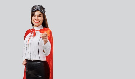 Cheerful woman wearing red cloak with aviator goggles holding arms crossed on gray backgroundの写真素材