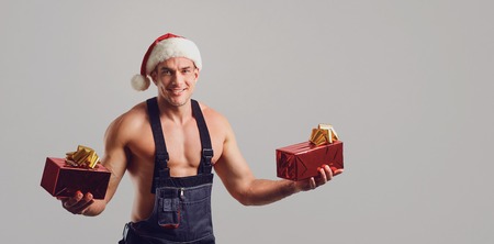 Repairman in Santa hat with a gift in special clothes with working tools on a gray background in Christmas.の写真素材