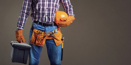 Faceless man in plaid shirt and gloves wearing utility belt and holding box of instruments and...