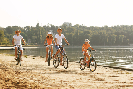 Adult parents with children riding bicycle on sandy shore of lake in beautiful natureの写真素材