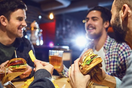 Happy friends eat burgers, drink beer in a bar. People in a fast food restaurant.の写真素材