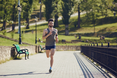 A male runner runs along the road to the park in the summer.の写真素材