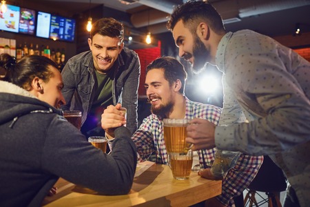 Friends make fun arm wrestling in a pub. Young people in a meeting in a pub.の写真素材