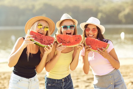 Girlfriends at a party eating a watermelon on the beach in the summer park.の写真素材