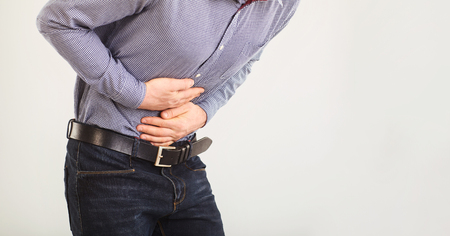 A man suffers from abdominal pain. Abdominal pain. The guy in the seeming clothes holding belly with hands.の写真素材