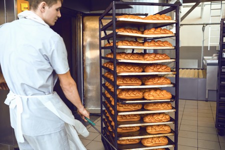 The baker pushes a tray with bread from the oven in the bakery manufactory.